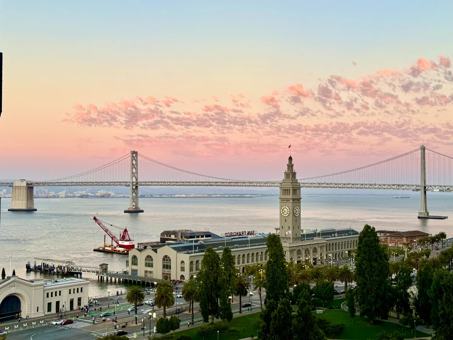 The Ferry Building and Bay Bridge beneath a pink sunset in San Francisco.
